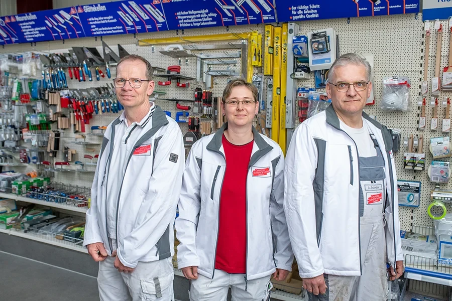 Mitarbeiter im Laden vor einer Werkzeugwand mit Arbeitskleidung