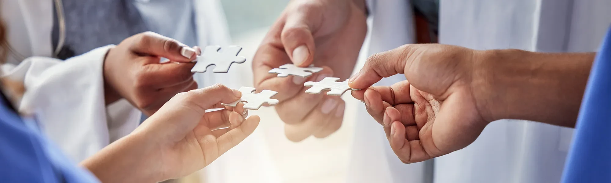 Mehrere Hände halten Puzzleteile als Symbol für Teamarbeit im medizinischen Bereich