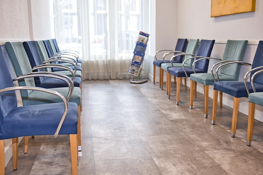 Wartezimmer einer Arztpraxis mit blauen Stühlen und Prospektständer, aerzte-galerie