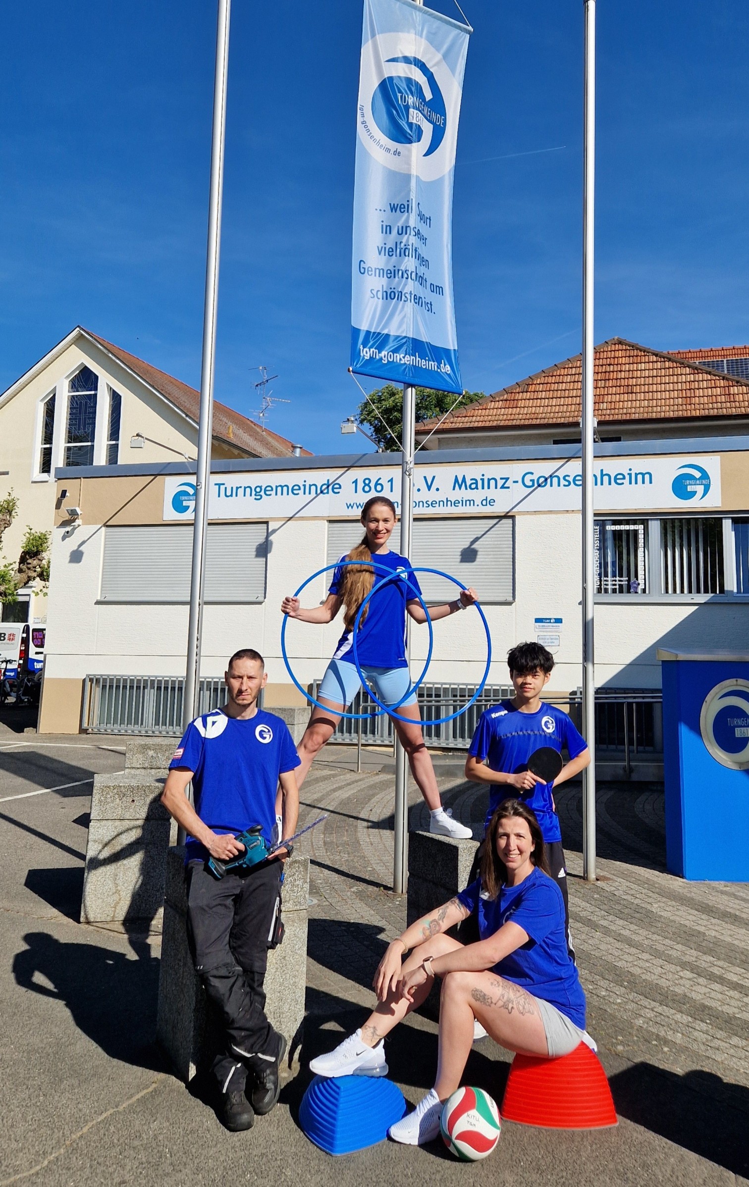 Mitglieder der Turngemeinde Mainz-Gonsenheim posieren vor dem Vereinsgebäude mit Sportgeräten.