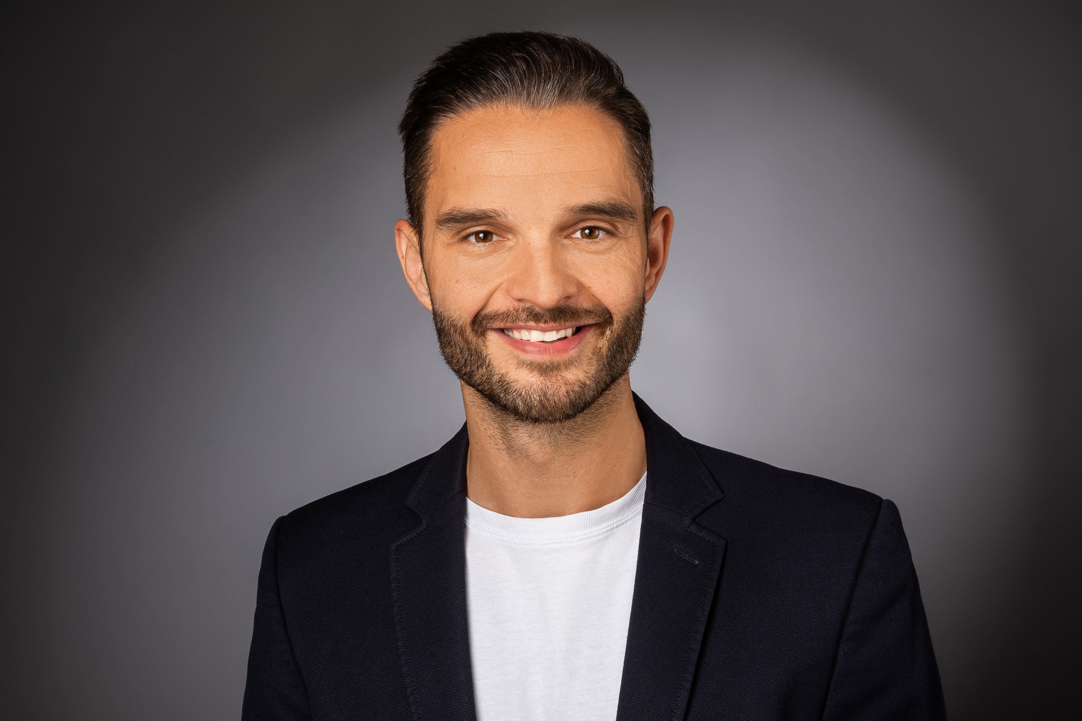 Porträt eines lächelnden Mannes im Anzug vor grauem Hintergrund