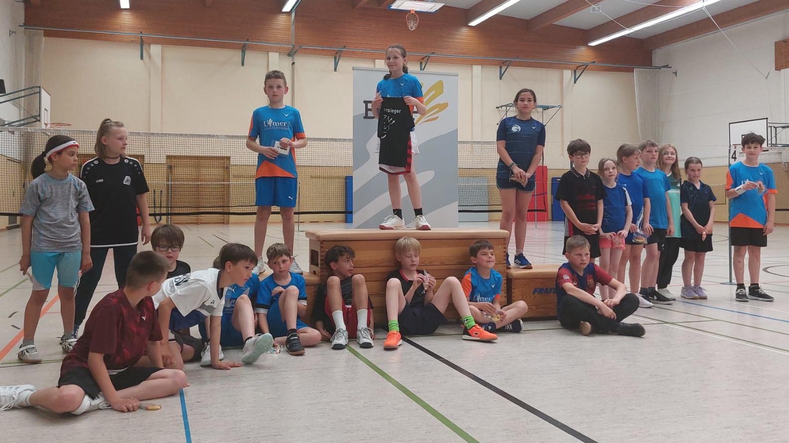 Kinder stehen und sitzen bei einer Siegerehrung in einer Turnhalle