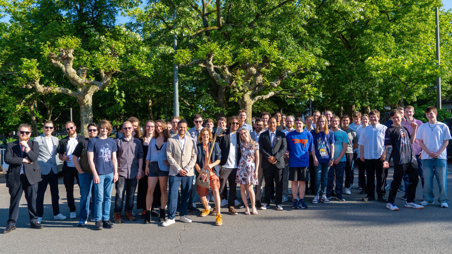 Gruppe von jungen Erwachsenen posiert draußen vor Bäumen bei sonnigem Wetter