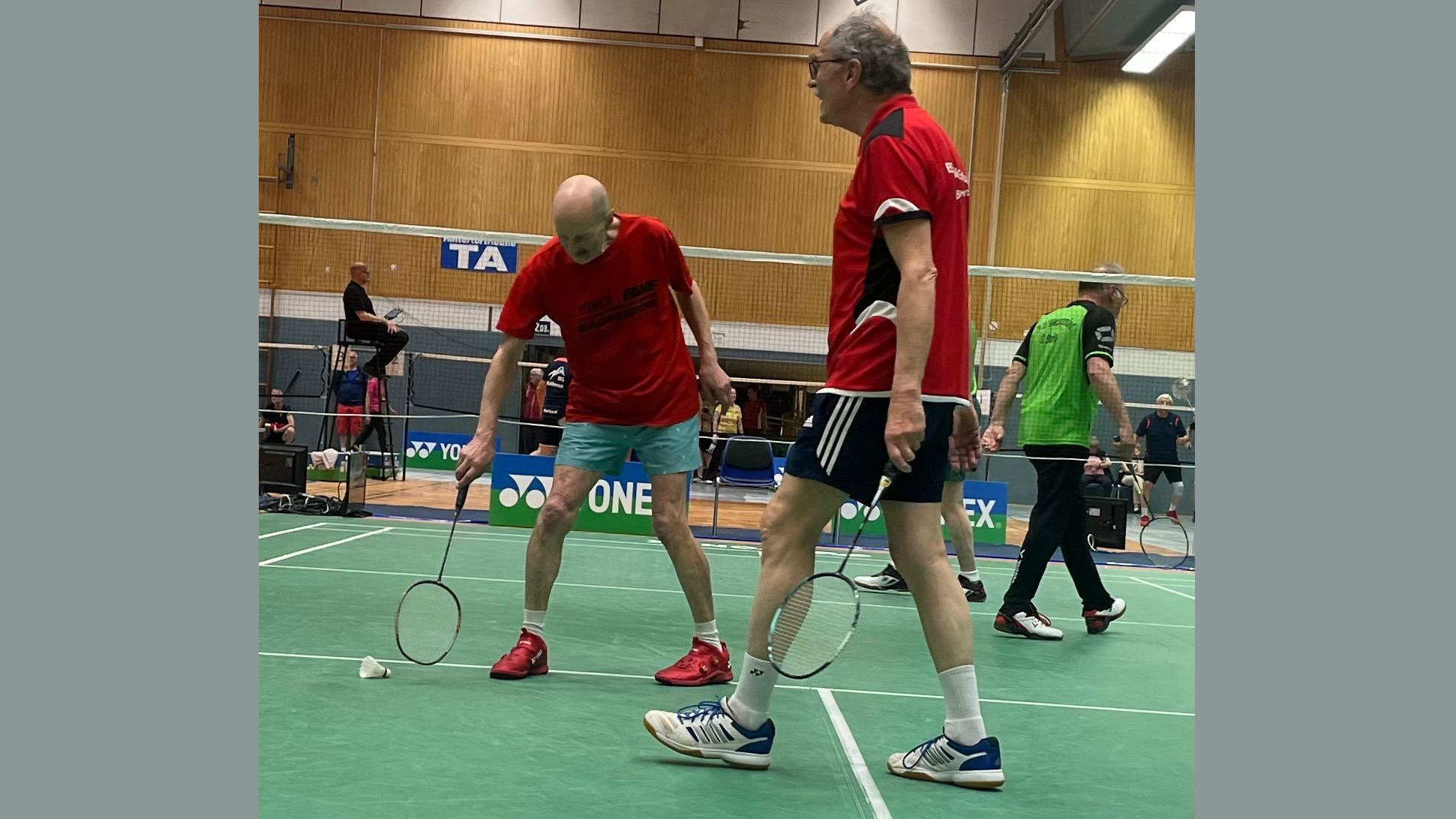 Zwei ältere Männer spielen Badminton in einer Turnhalle