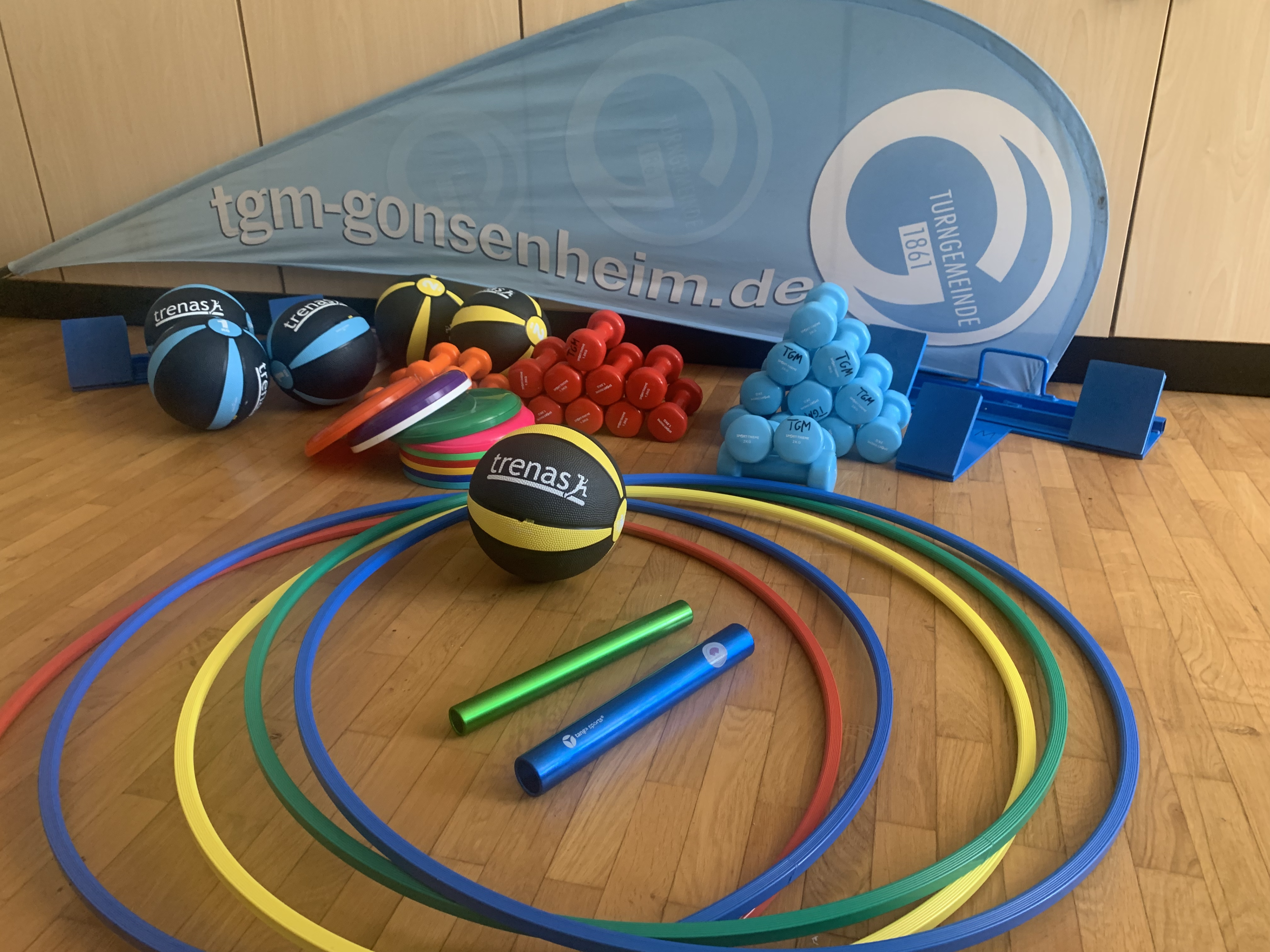 Verschiedene Sportgeräte bei TGM Gonsenheim, darunter Hanteln, Medizinbälle und Reifen.