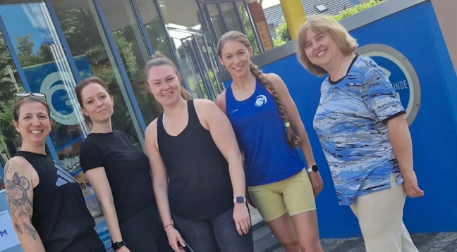 Eine Gruppe von Frauen in sportlicher Kleidung steht vor einem modernen Gebäude.