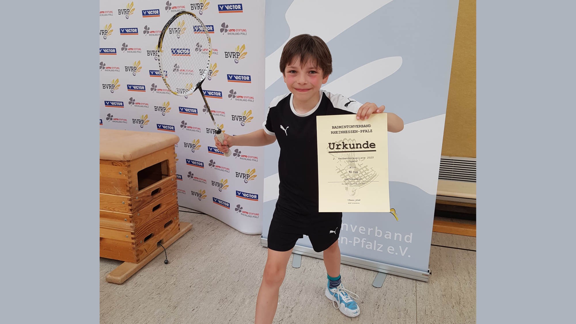 Junger Badminton-Spieler hält Urkunde und Schläger