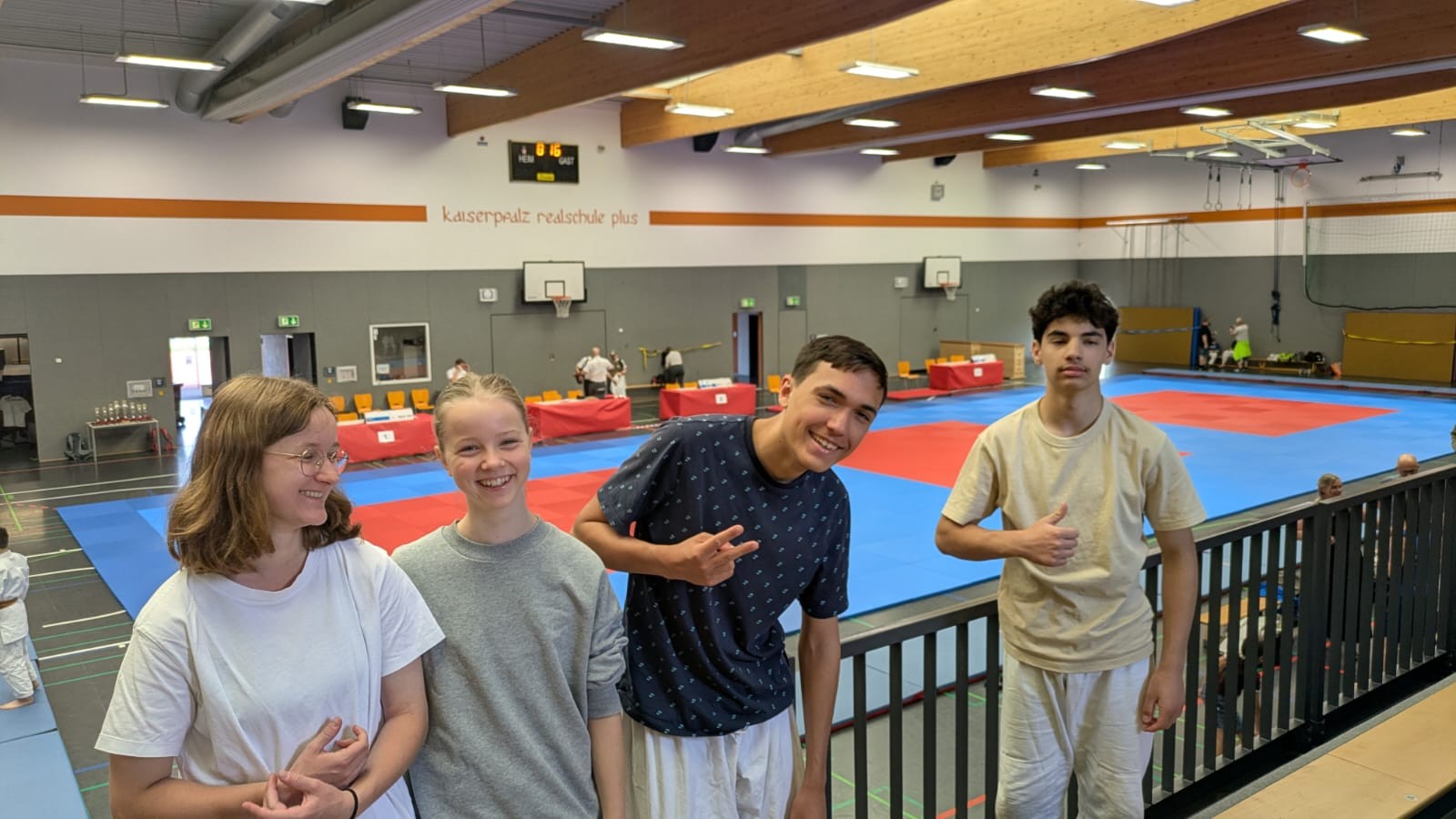 Jugendliche lächeln in einer Sporthalle mit Judomatten im Hintergrund.