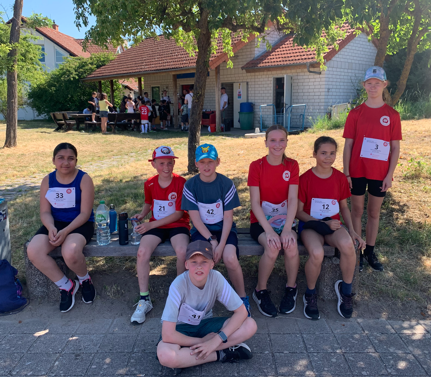 Gruppe von Kindern in Sportkleidung auf einer Gartenbank sitzend.