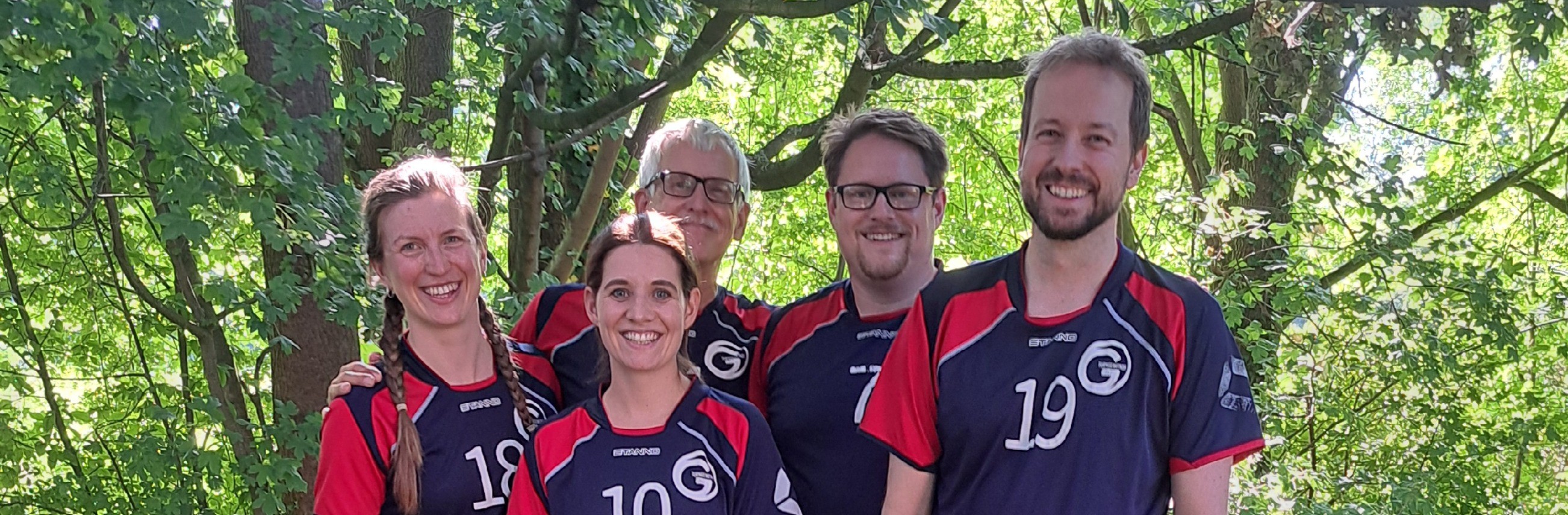 Lächelnde Volleyball-Teammitglieder im Freien vor grünen Bäumen