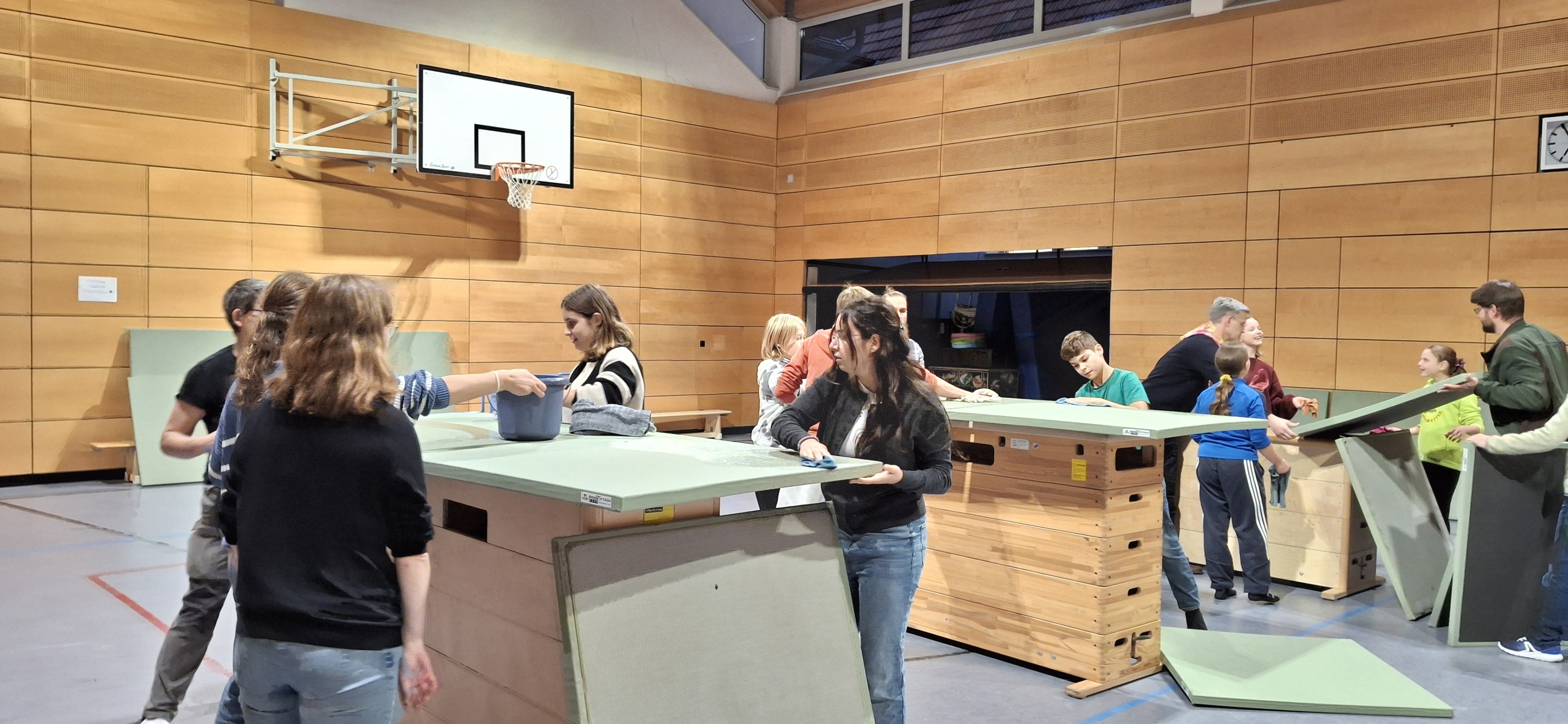 Mehrere Personen reinigen Turngeräte in einer Sporthalle