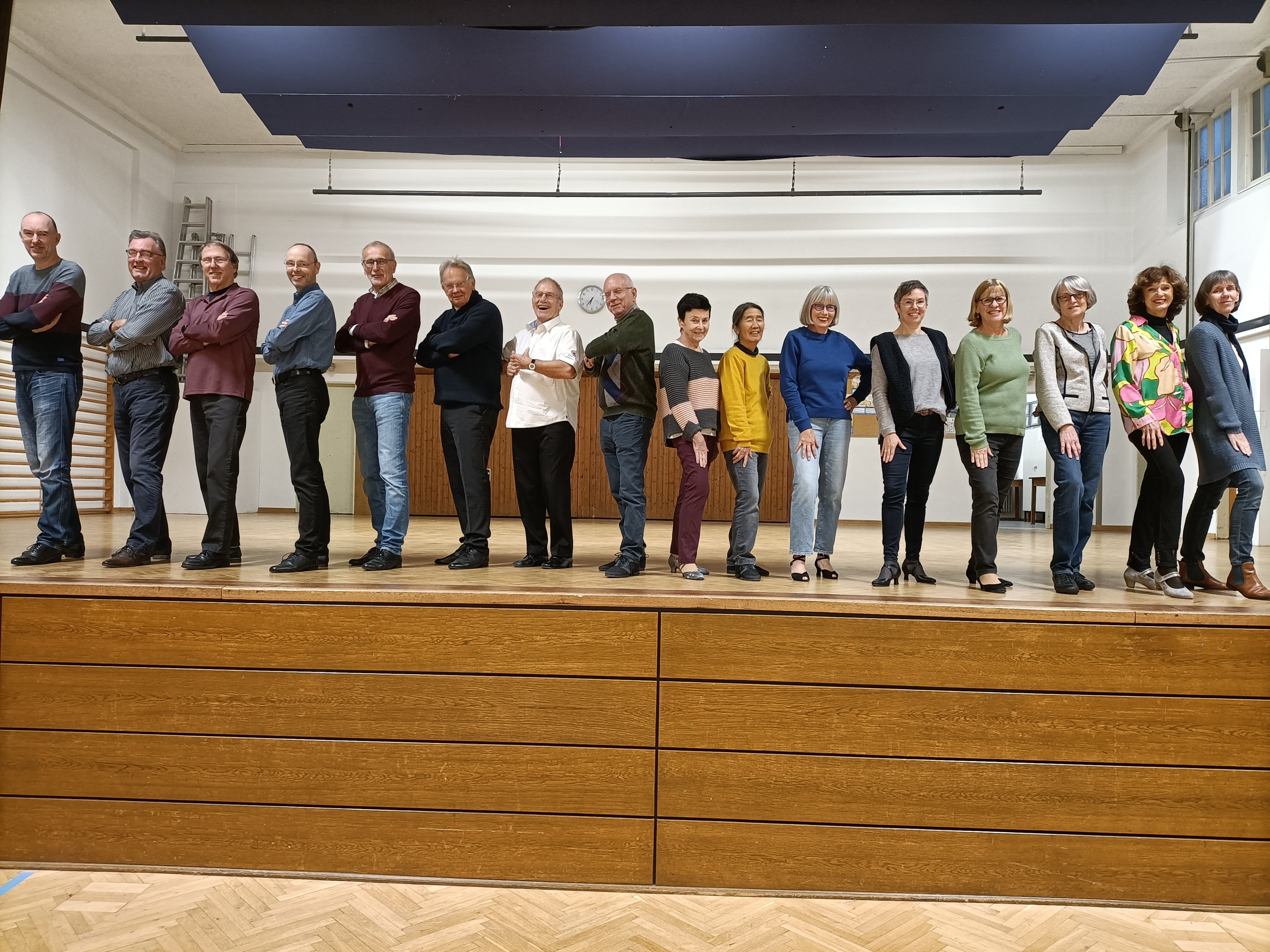 Gruppe von Menschen steht auf einer Bühne in einem Saal, verschiedene Altersgruppen, Indoor-Aufnahme