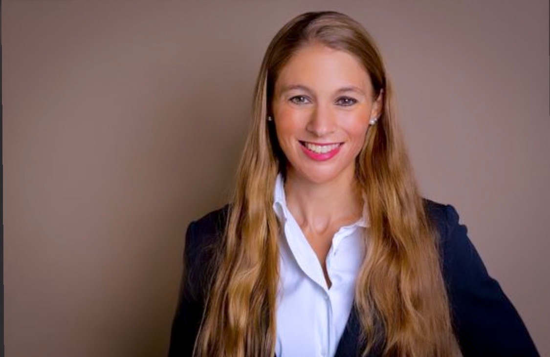 Frau mit langen blonden Haaren im Business-Outfit vor neutralem Hintergrund
