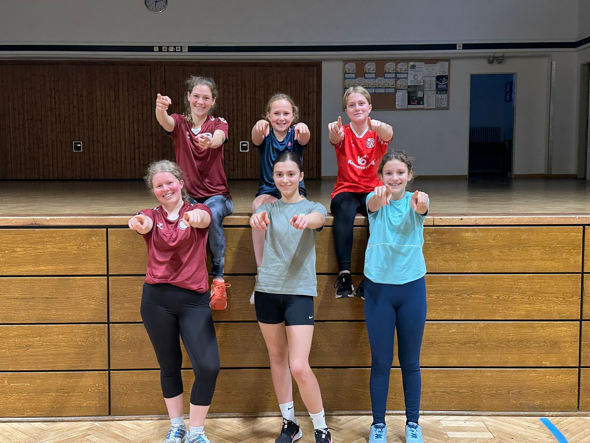 Gruppe von Jugendlichen beim Sport in einer Turnhalle, alle zeigen mit den Armen nach vorne