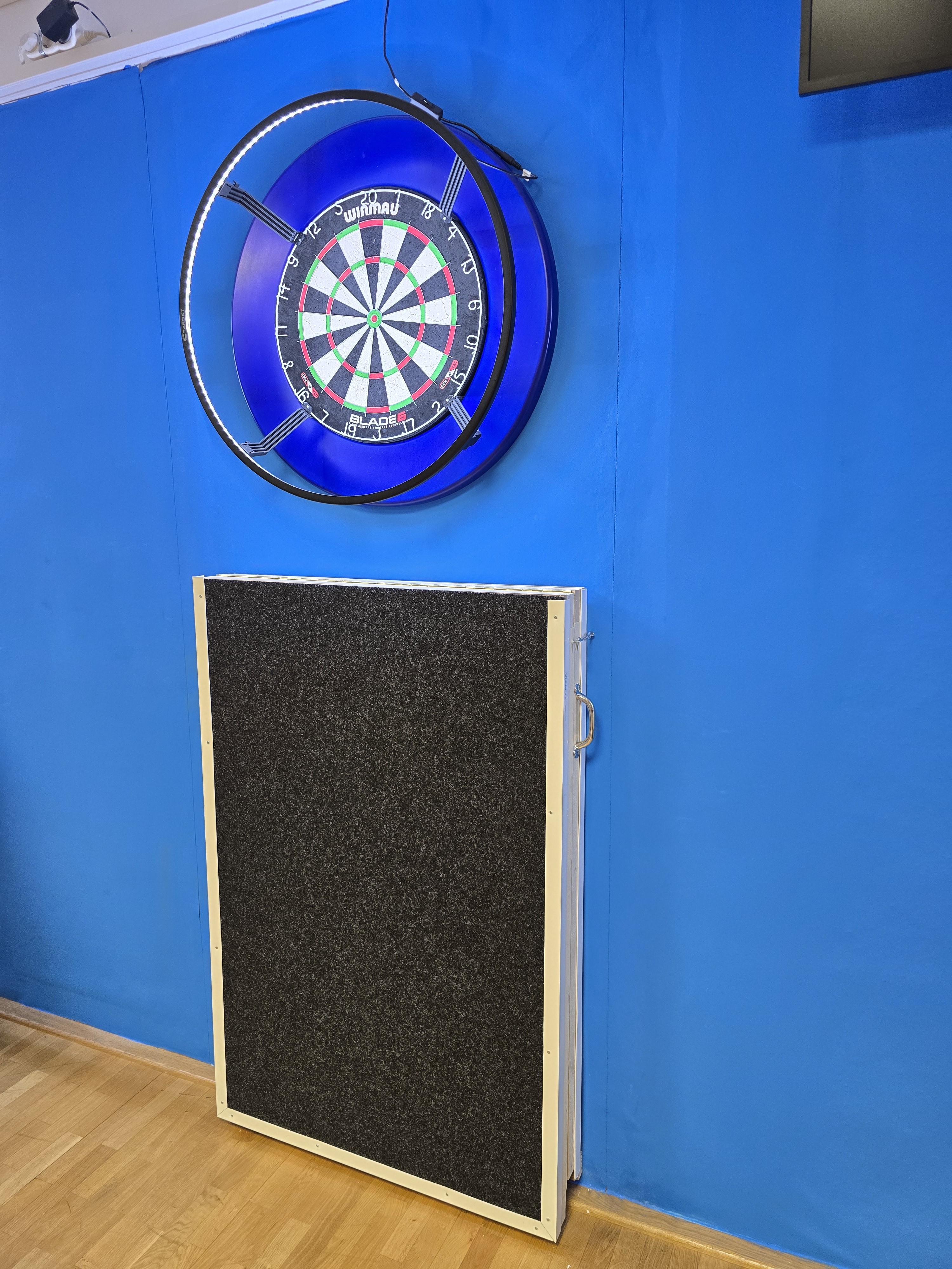 Dartboard Winmau Blade 6 an blauer Wand mit Schutzunterlage darunter, aufgenommen am 27.10.2025