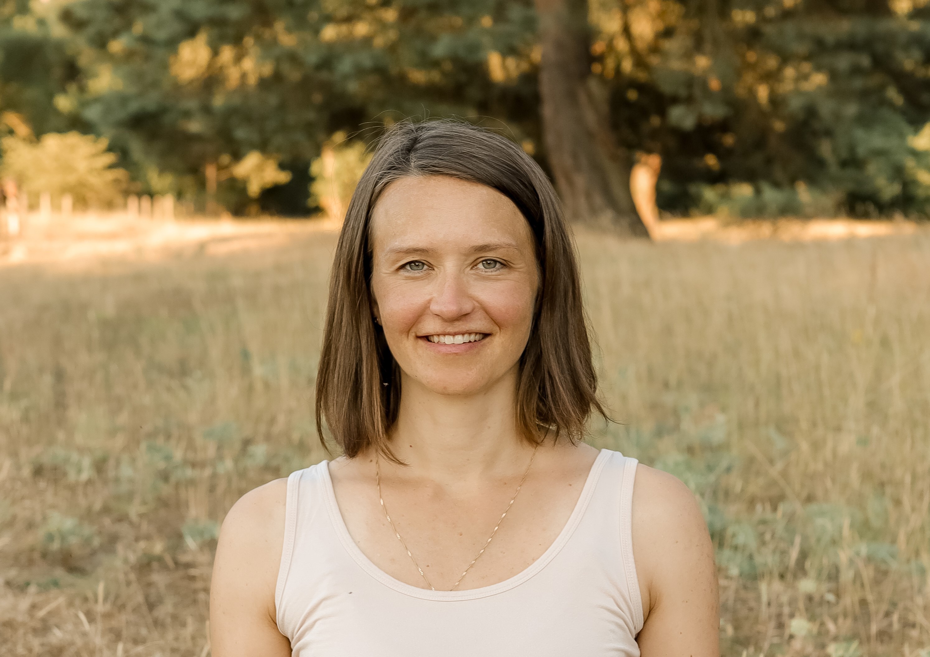 Frau mit braunen Haaren im ärmellosen Top auf einer Wiese vor Bäumen