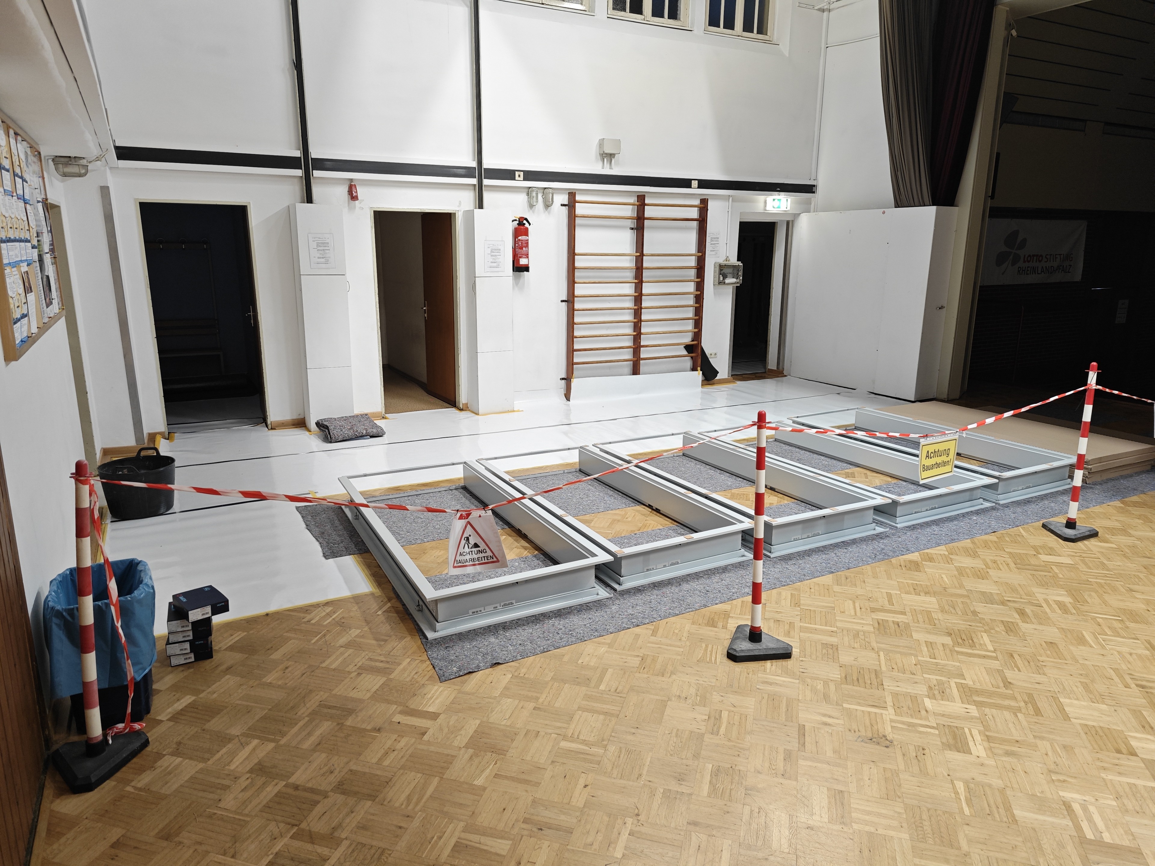 Baustelle in einer Turnhalle mit Absperrband und Warnschildern, Bodenarbeiten im Innenraum