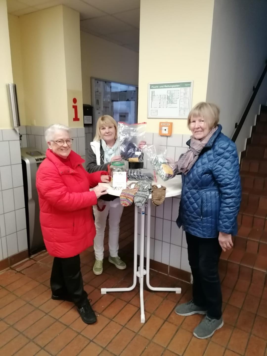 Drei Frauen präsentieren handgestrickte Socken auf einem Tisch im Eingangsbereich, socken-2025