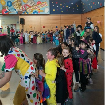 Kinderreihe beim Kindermaskenball in einer bunt geschmückten Halle mit verkleideten Kindern