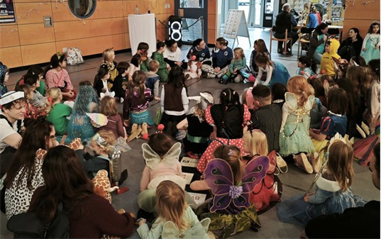 Kinder sitzen im Sitzkreis beim Kindermaskenball, verkleidet in bunten Kostümen