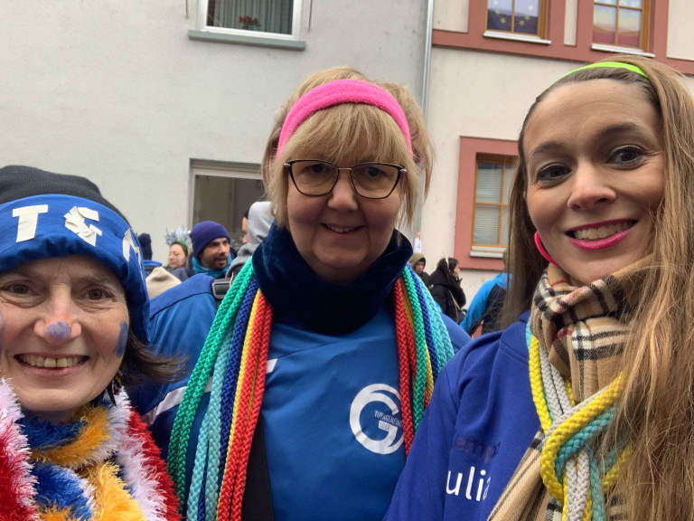 Menschen in blauer Kleidung feiern draußen bei einem Straßenumzug, tragen bunte Schals und Kostüme