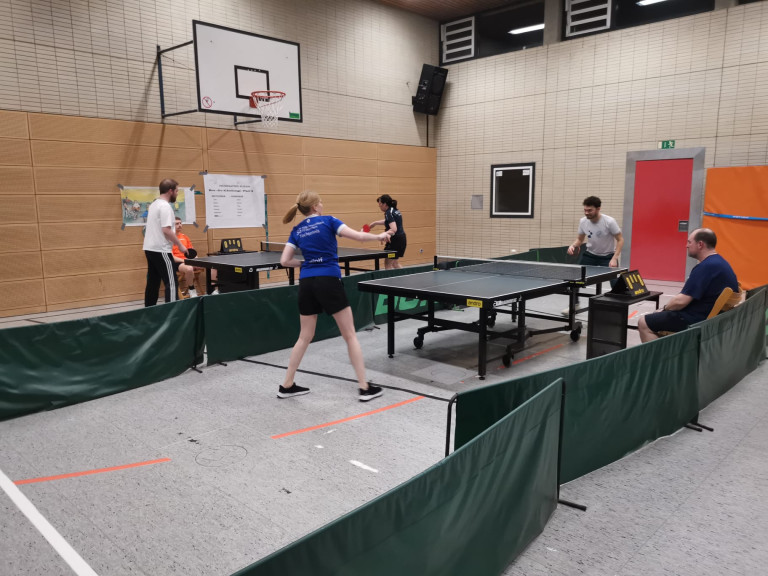 Tischtennis Einzelspiel in einer Sporthalle mit mehreren Spielern und Zuschauern