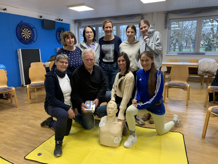 Modul 2 Erste-Hilfe-Kurs 2026 – Teilnehmer üben Wiederbelebung mit Defibrillator Gruppe bei Modul 2 eines Erste-Hilfe-Kurses 2026 mit Übungspuppe und Defibrillator