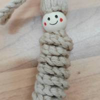 Makramee-Figur mit lächelndem Gesicht auf Holzuntergrund