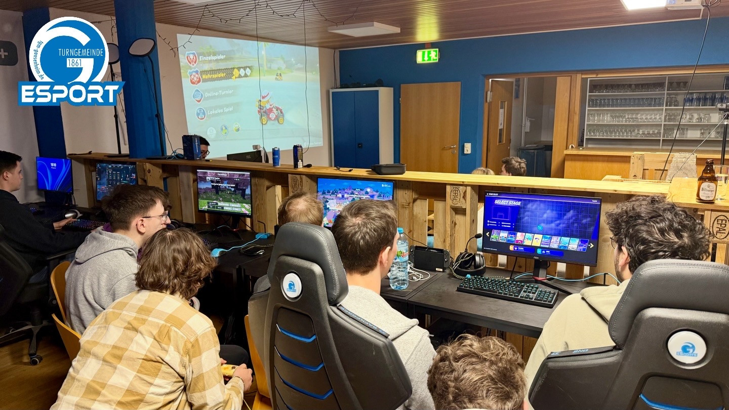 Mehrere junge Leute spielen Videospiele bei einem Gaming-Event mit mehreren Monitoren und Konsolen in einem modernen Raum.