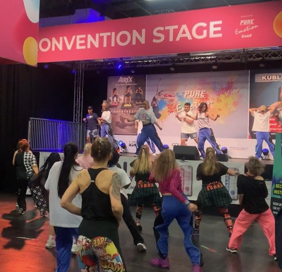 Tanzworkshop auf der Convention Stage bei der Pure Emotion GmbH, Teilnehmer tanzen vor einer Bühne mit Choreografen