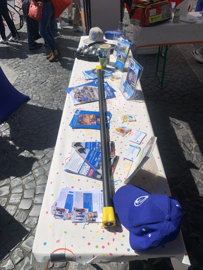 TGMGO Messestand mit Informationsmaterial, Flyern und Werbeartikeln auf einem Tisch im Freien