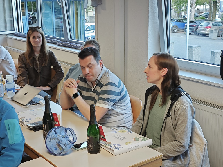 Gruppe von Menschen bei einem Treffen am Tisch mit Sektflaschen und Geschenken am 23. April 2026