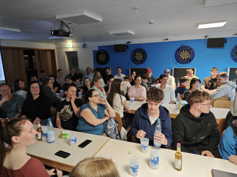 Gruppe von Menschen bei einem Treffen oder Event in einem Raum mit Dartscheiben, aufgenommen am 23.04.2026