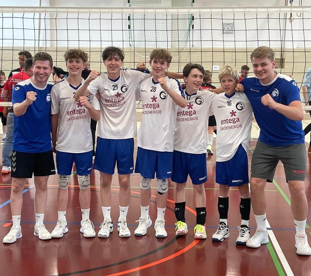 Junges Volleyballteam jubelt in Sporthalle nach dem Spiel, Spieler tragen Trikots mit Entega Ökoenergie Logo