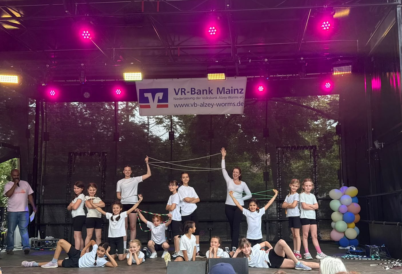 Kindergruppe bei einer Aufführung auf einer Bühne mit VR-Bank Mainz Banner im Hintergrund