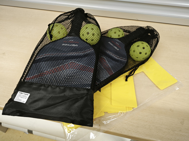 Pickleball-Schläger und Bälle im Netzbeutel auf einem Tisch