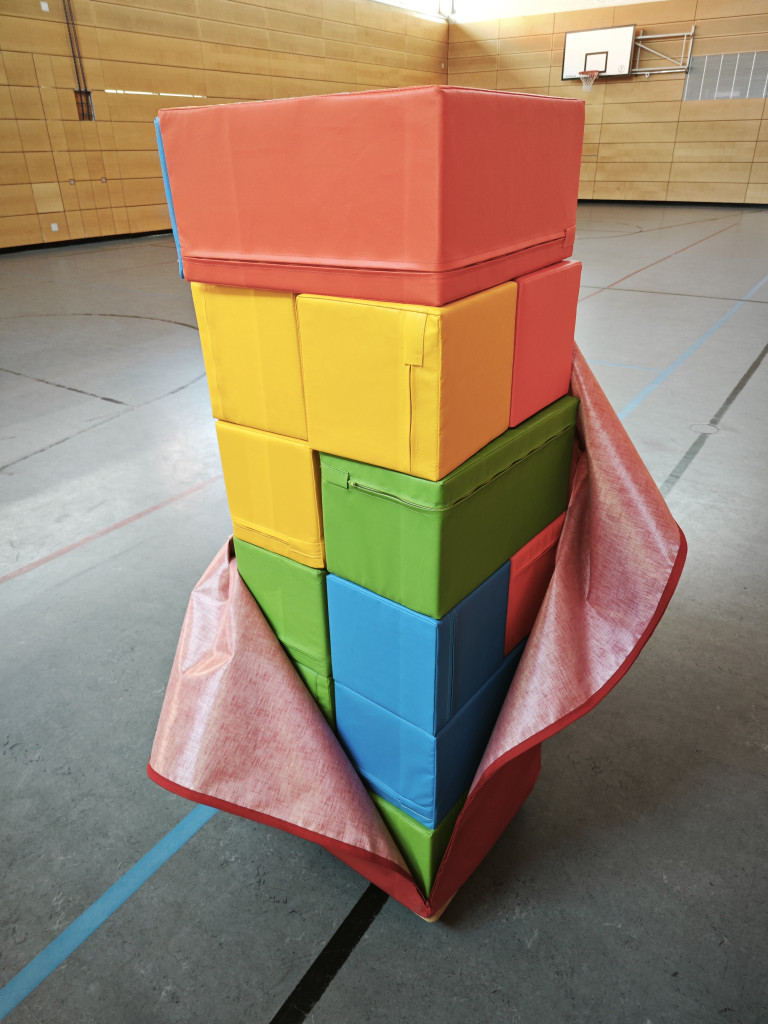 Bunte Schaumstoffbausteine in einer Turnhalle, teilweise mit roter Matte umwickelt