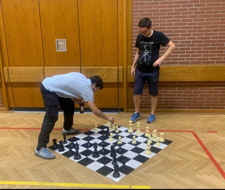 Zwei Männer spielen Schach auf einem großen Schachbrett in einer Turnhalle