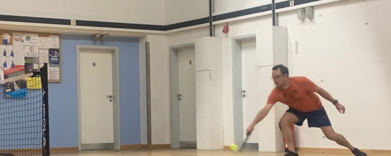 Person spielt Tennis in einer Halle mit gelbem Ball
