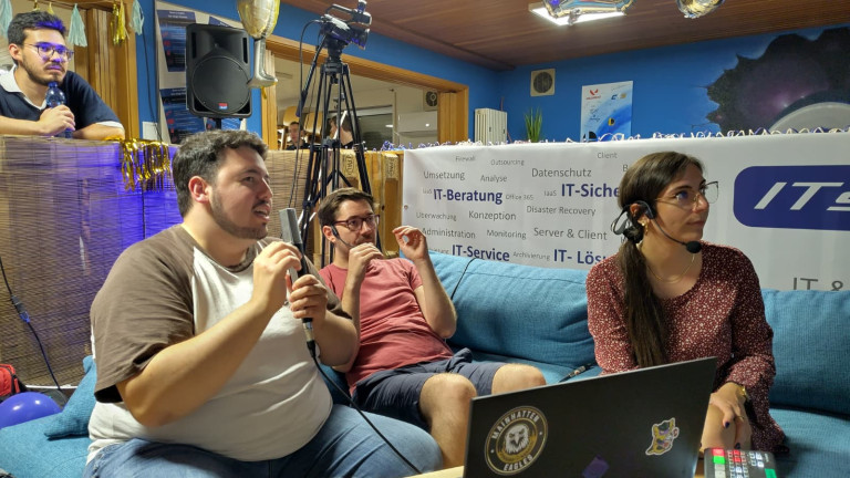 IT-Beratung und IT-Sicherheit Veranstaltung am 28.08.2026 – Menschen diskutieren Technik und IT-Lösungen Menschen bei einer IT-Beratung oder IT-Sicherheitsveranstaltung auf einem Sofa, Mikrofone und Technik im Vordergrund, Banner mit IT-Service und IT-Lösungen im Hintergrund.