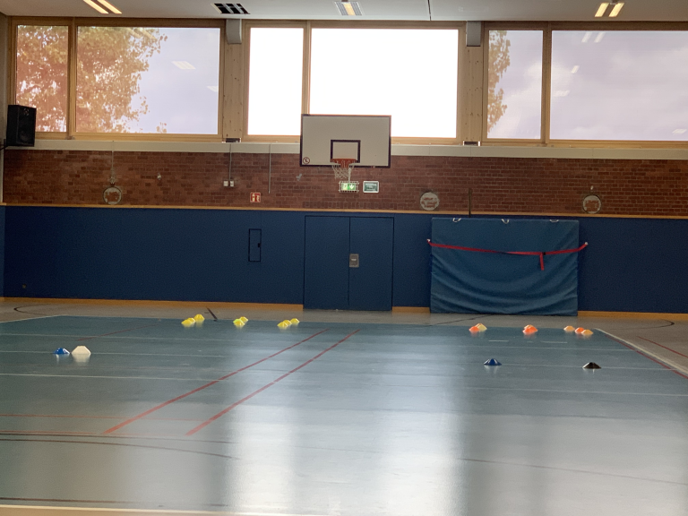 Kreative Stundeneinstiege im Sportunterricht: Turnhalle mit aufgebauten Markierungshütchen und Basketballkorb
