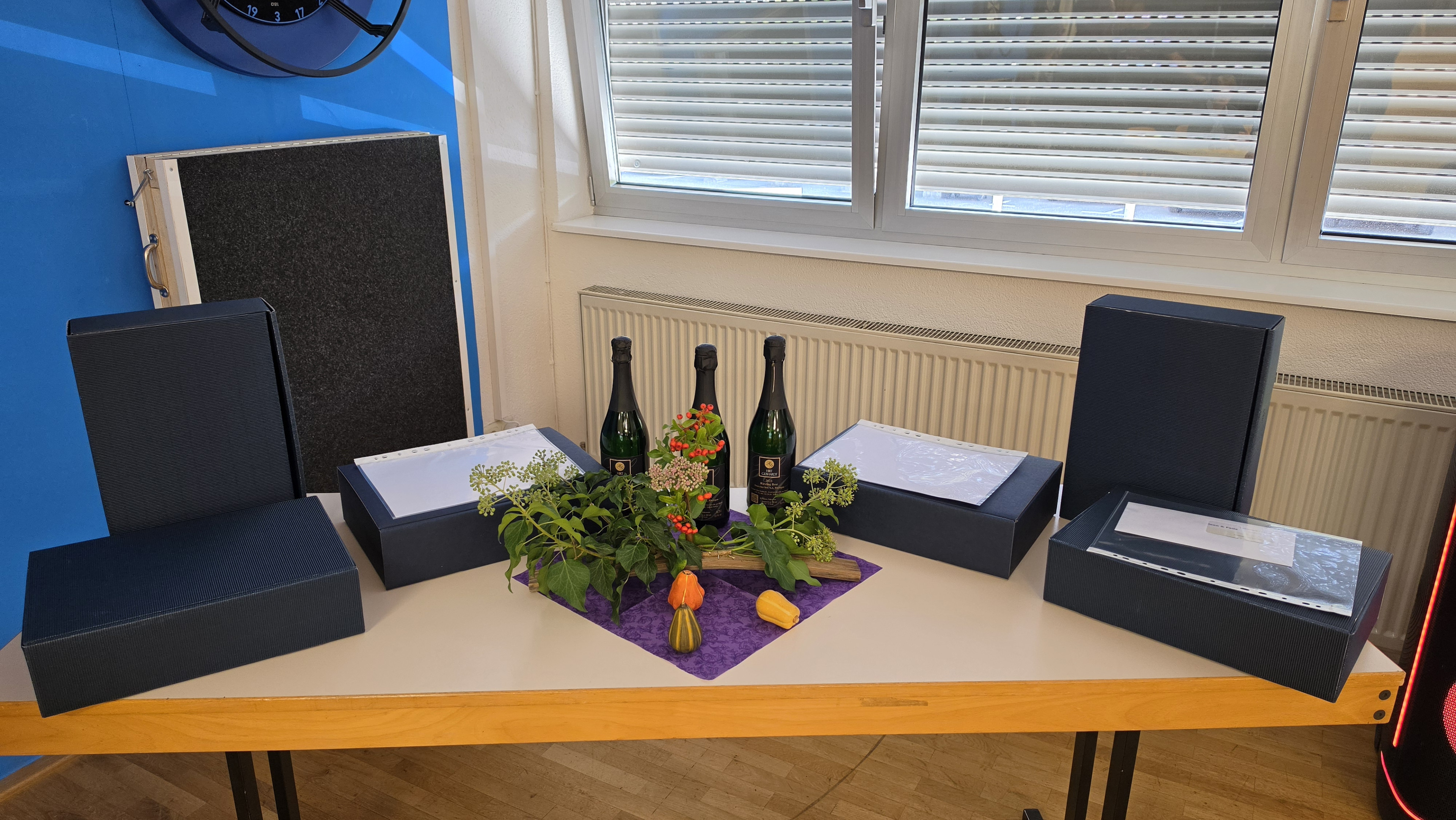 Geschenkübergabe mit Sektflaschen, Geschenkboxen und herbstlicher Dekoration auf einem Tisch am 17.09.2026