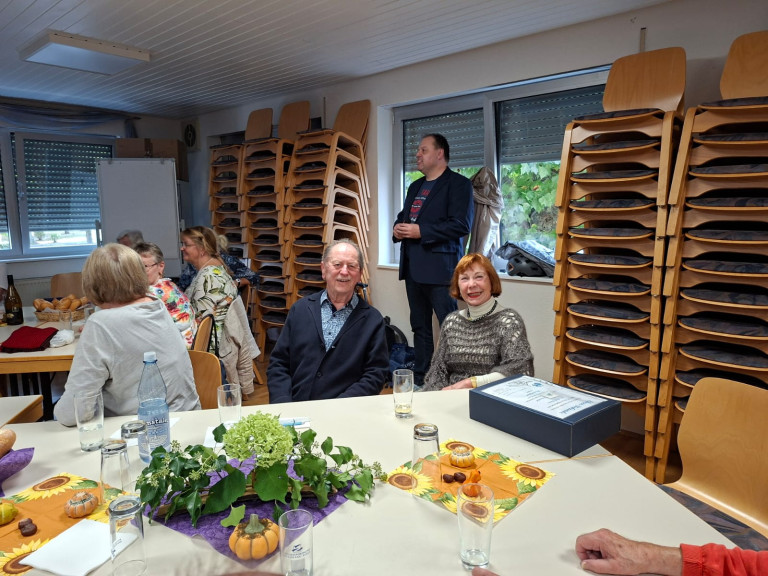 Gesellige Runde älterer Menschen bei einer Veranstaltung in einem Gemeinschaftsraum mit herbstlicher Dekoration