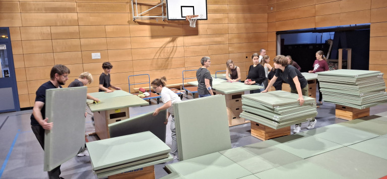 Gemeinsamer Aufbau von Turnmatten in einer Sporthalle am 28.09.2026 Mehrere Personen bauen gemeinsam Turnmatten in einer Sporthalle auf, im Hintergrund ein Basketballkorb.