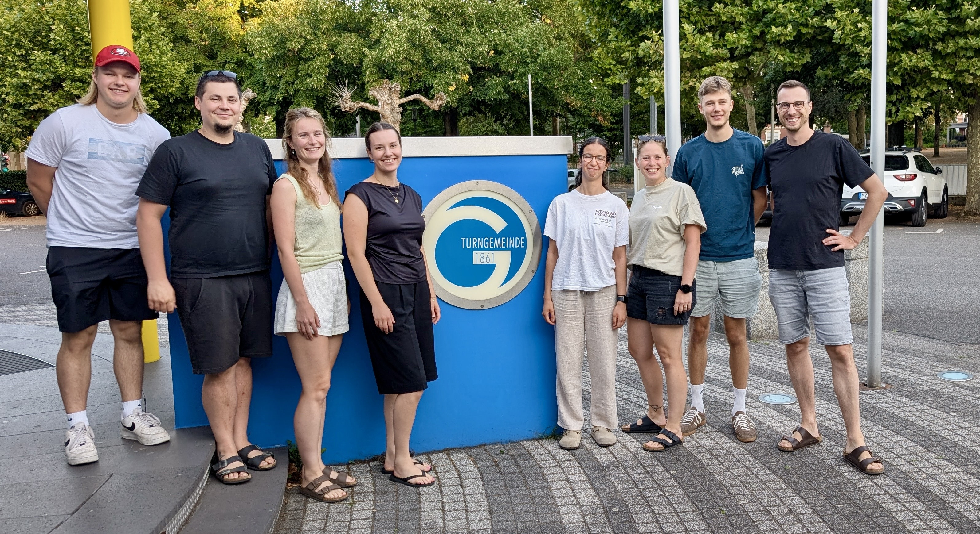 Abteilungsleitung Volleyball der Turngemeinde 1861 steht gemeinsam vor dem Vereinslogo