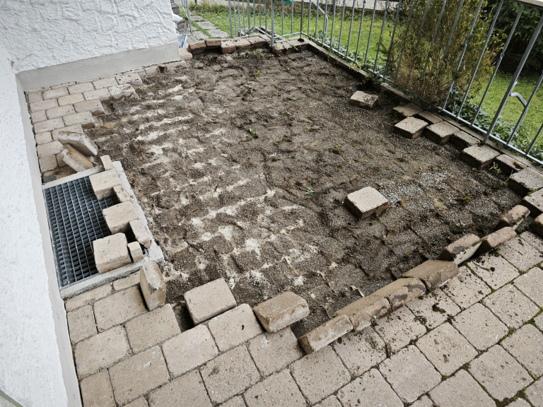 Baustelle Terrasse mit teilweise entfernten Platten und Erdarbeiten – Vorbereitung für Terrassensanierung Teilweise entfernte Terrassenplatten auf einer Baustelle im Garten, Vorbereitungen für eine neue Terrasse oder Sanierung.