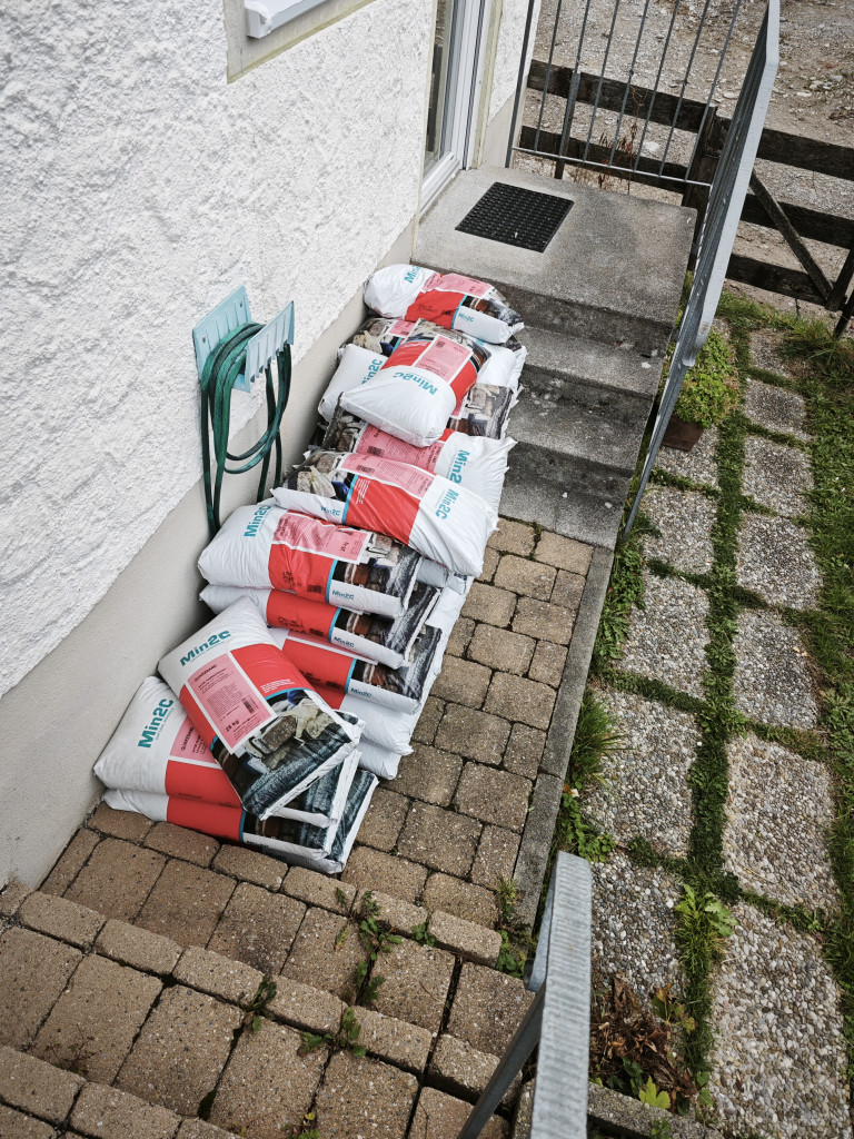 Gestapelte Min2C Zementsäcke auf Terrasse neben Hauswand Mehrere Säcke Min2C Zement auf einer Terrasse neben einer Hauswand gestapelt