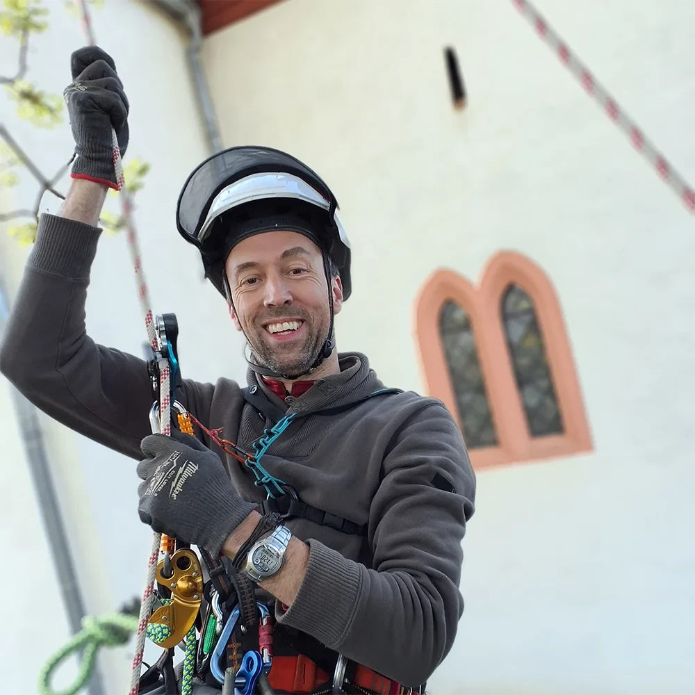 Boris Kramer bei der Seilarbeit vor einer Kirche, ausgestattet mit Kletterausrüstung und Helm
