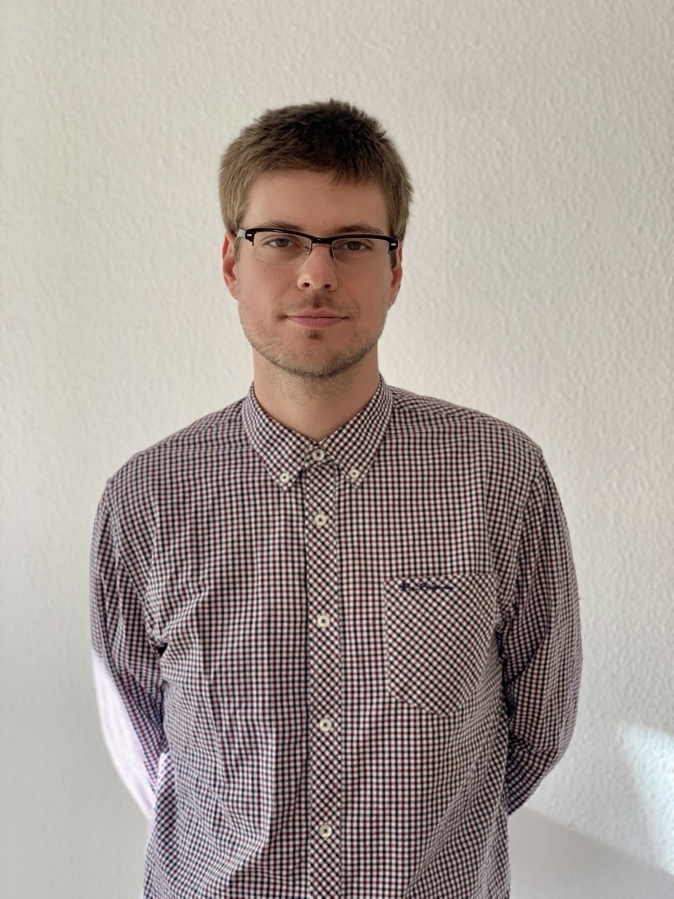 Angel Ponow mit kariertem Hemd vor weißer Wand