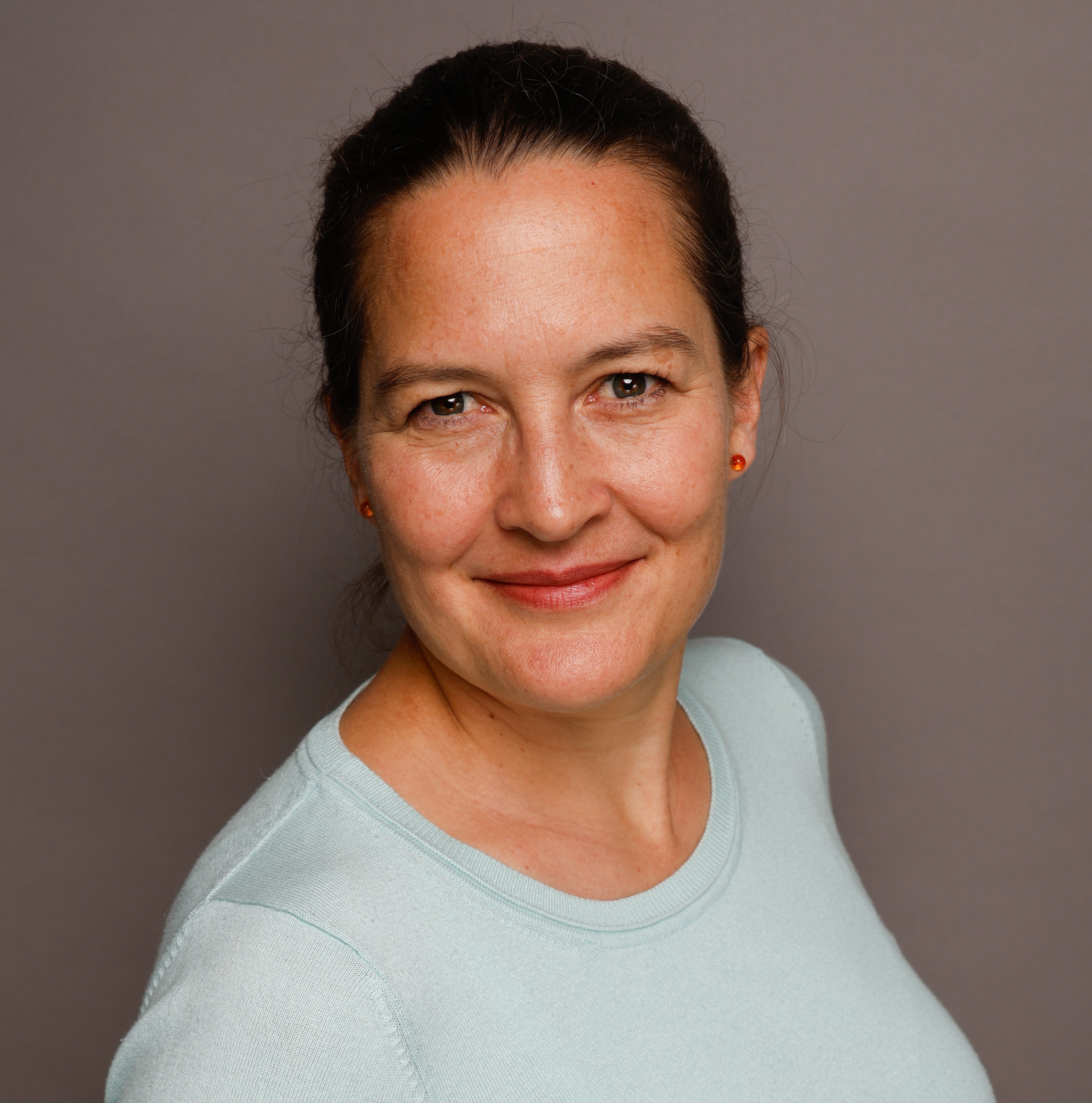 Porträt einer Frau mit hellblauem Pullover vor grauem Hintergrund, Raimer